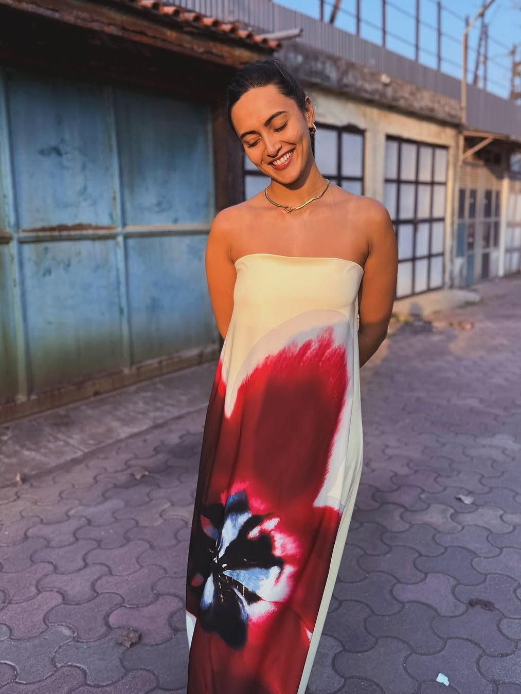 Cream strapless backless tube maxi dress with bold red floral print and blue-black bloom, worn by smiling woman.