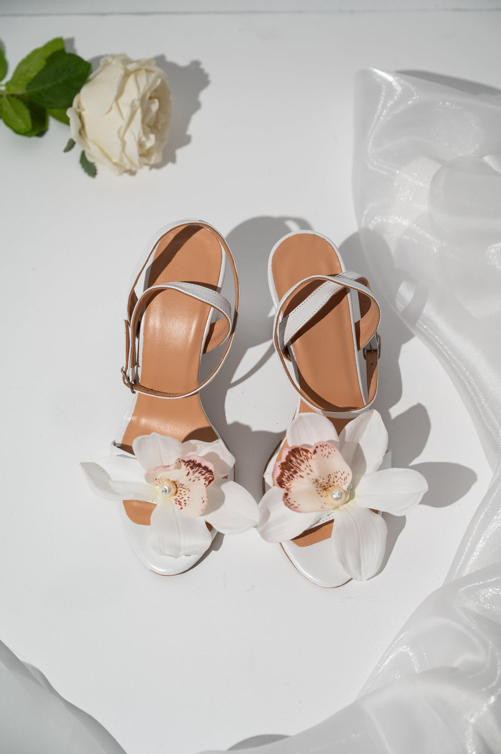 Pair of high-heeled sandals with floral decorations on a white surface.
