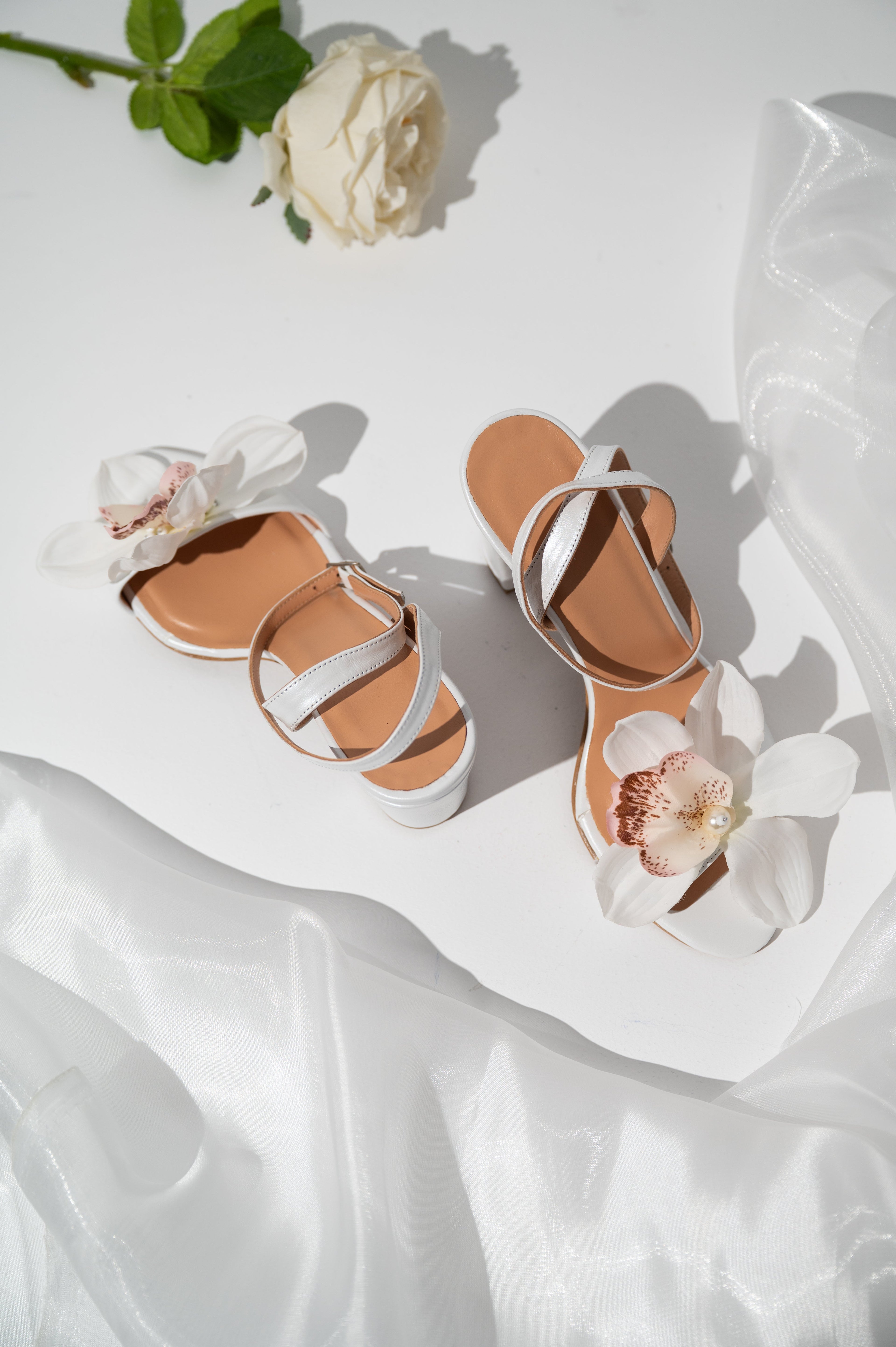Pair of sandals with white straps on a white fabric background with flowers.