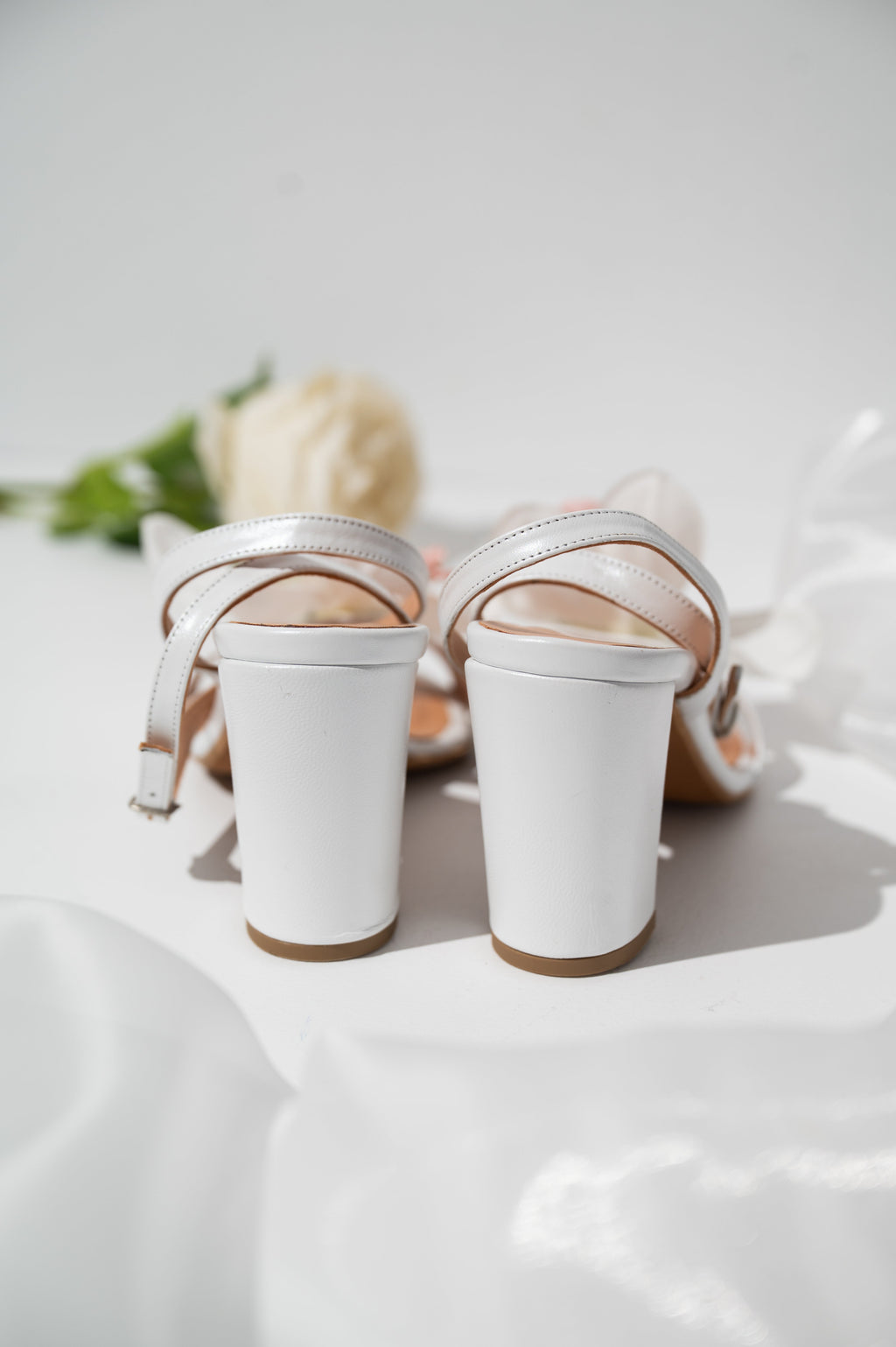 White high-heeled shoes with thin straps on a light background