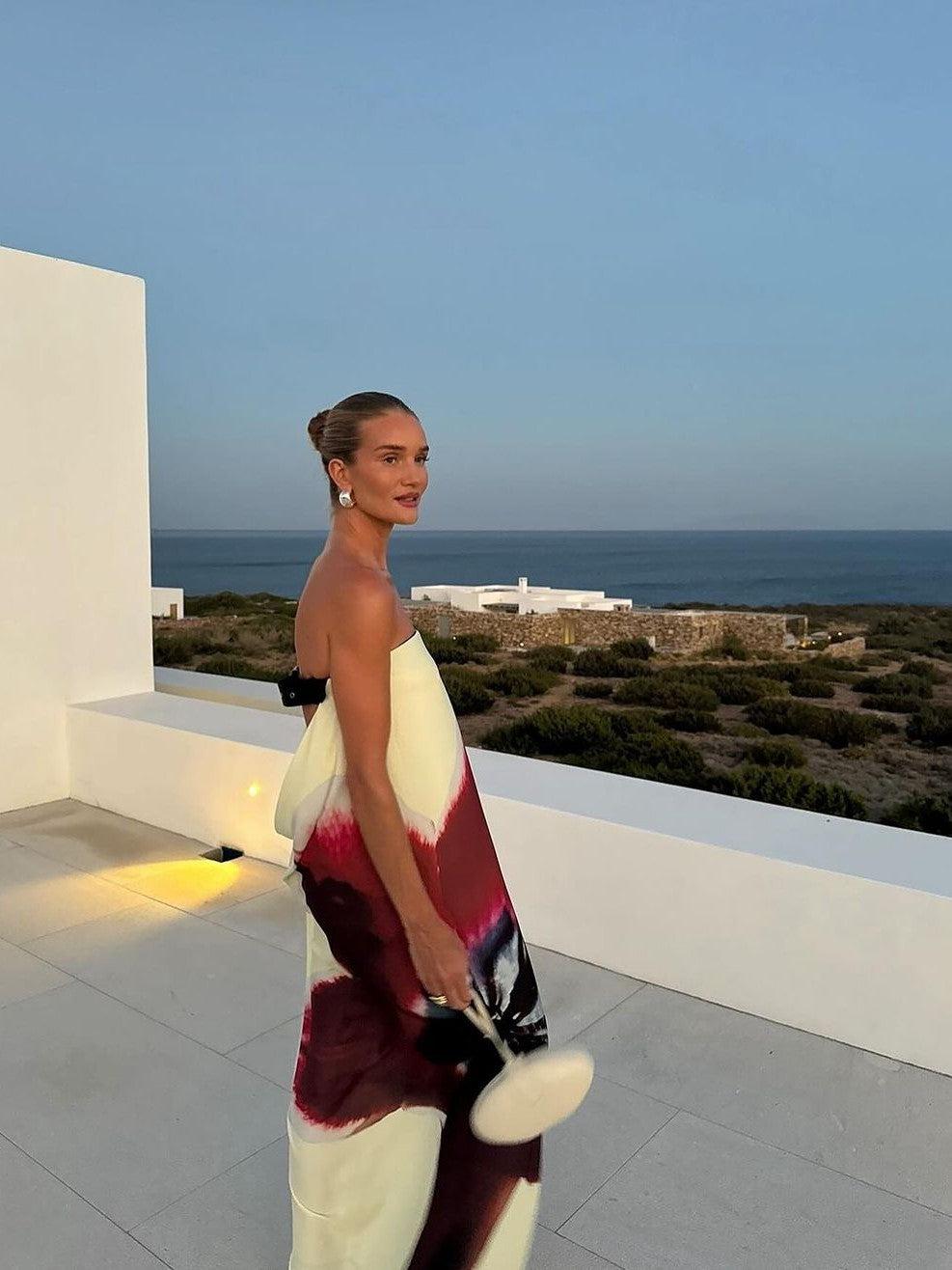 Strapless backless maxi dress with cream, burgundy and black abstract print, worn by a model on a sea-view rooftop.