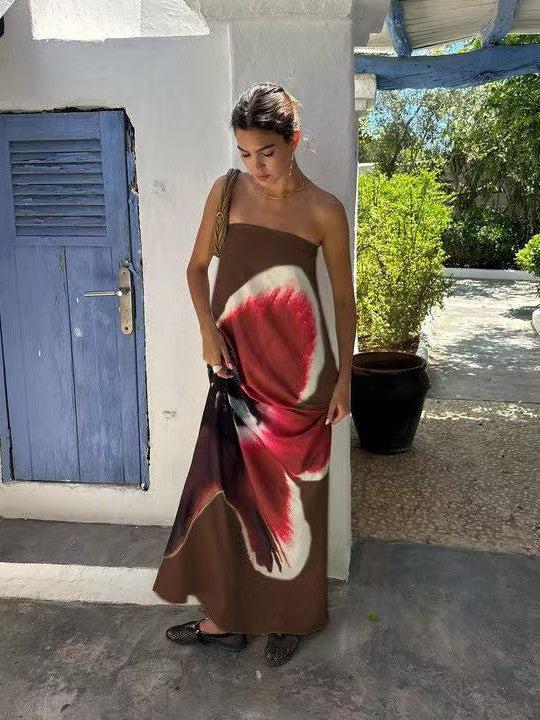 Brown strapless backless tube maxi dress with red floral print; woman in black sandals stands beside blue door.