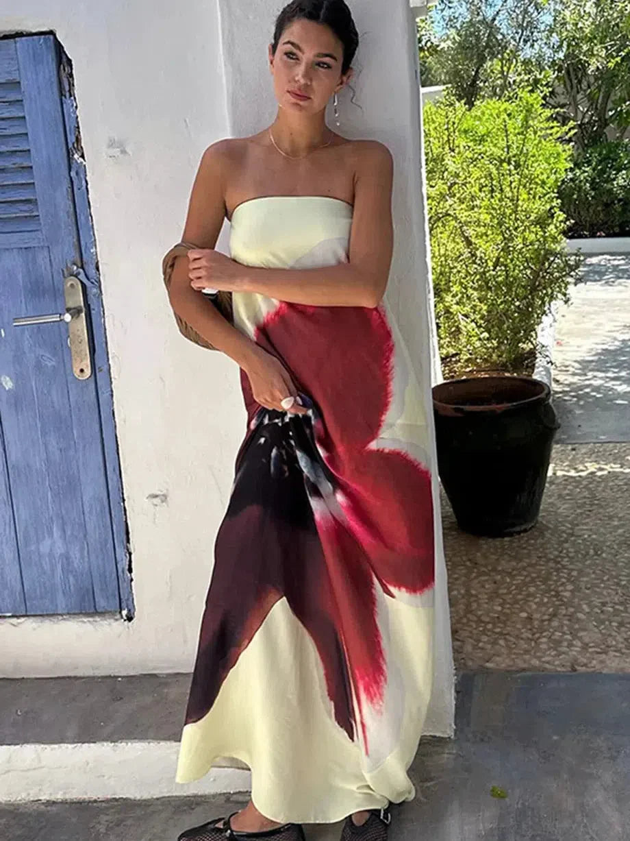 Woman in cream strapless maxi dress with red and burgundy floral print, standing by a white wall and blue door.