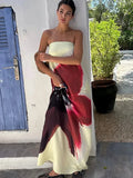 Woman in cream strapless maxi dress with red and burgundy floral print, standing by a white wall and blue door.