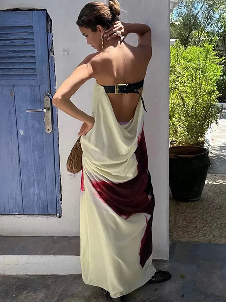 Back view of a woman wearing pale yellow draped backless maxi dress with burgundy accents, black belt and gold buckle.